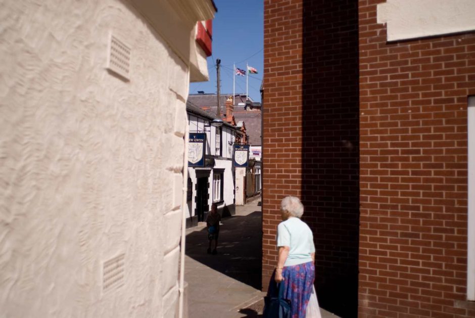 Kleurfoto van een oudere dame die door een smalle straat wandelt