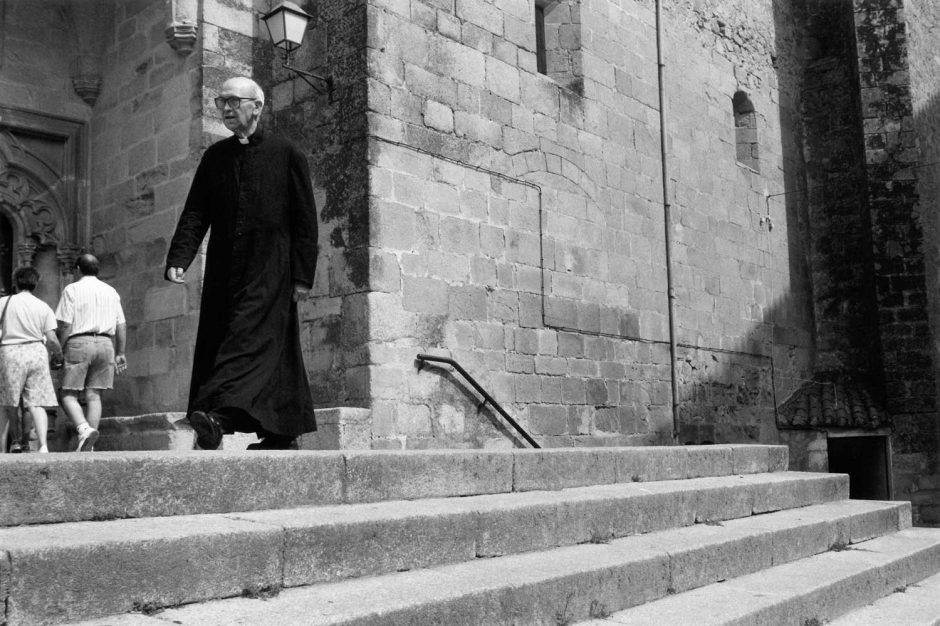 Zwart-wit foto van een priester op de trappen van zijn kerk