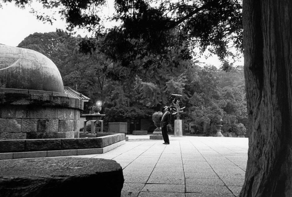 Zwart-wit foto van een man die zijn ogen beschermt en opkijkt naar de grote buddha