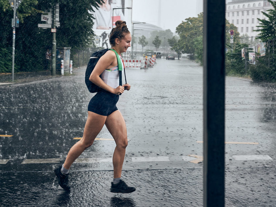 Kleurfoto van een jonge dame die in zomer outfit door de regen rent