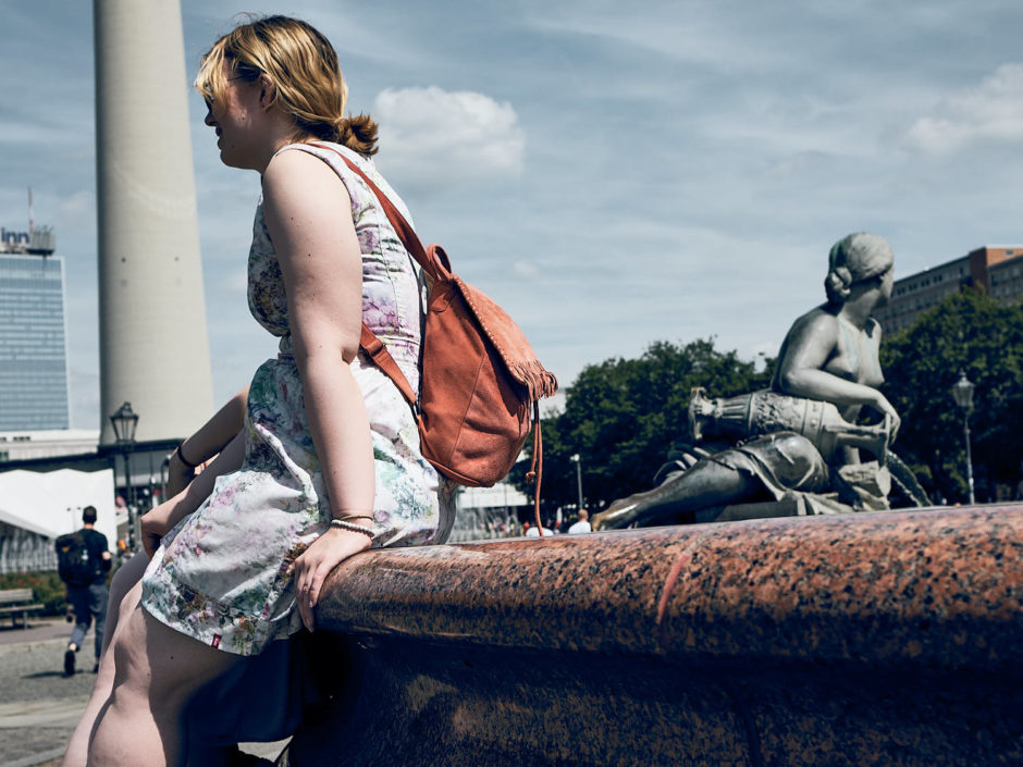 Kleurfoto van een jonge dame met het haar opgestoken, net zoals het beeld op de achtergrond