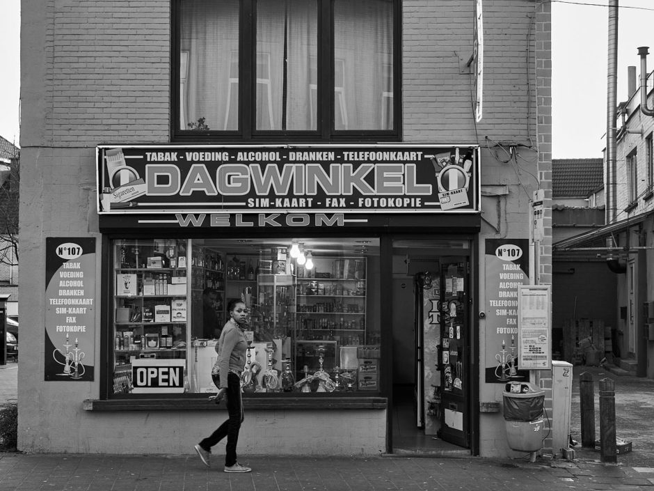 Zwart-wit foto van een jonge dame voor de gevel van een dagwinkel in de Phoenixstraat in Gent