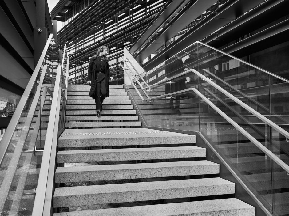 Zwart-wit foto van een donker geklede jonge dame met koptelefoon op de trappen naar bibliotheek De Krook