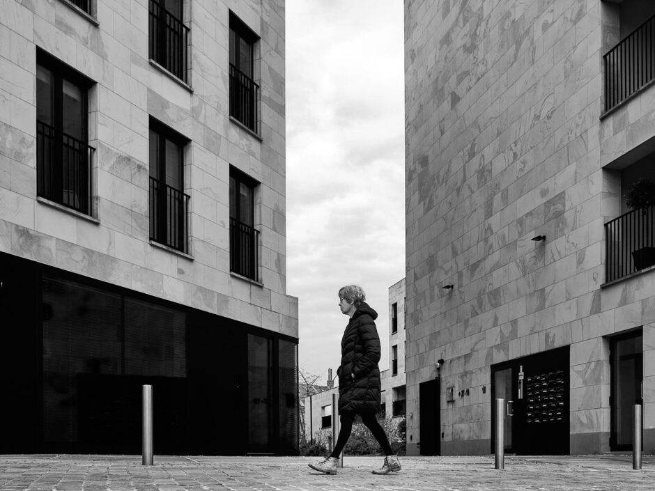 Black & white street photography of homo urbanus, more precisely a lady in between two housing blocks