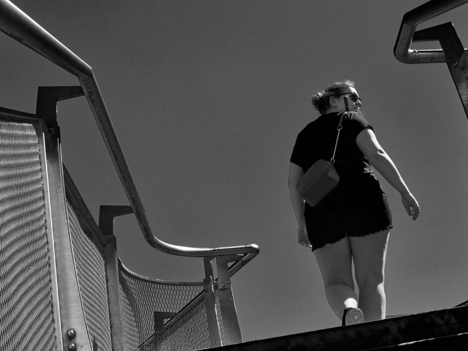 Black & white street photography of homo urbanus, more precisely of a woman looking over her shoulder in front of a blue sky backdrop