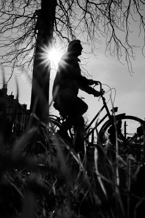 Black & white street photography of homo urbanus, more precisely of a man on a bicycle in back light sunburst