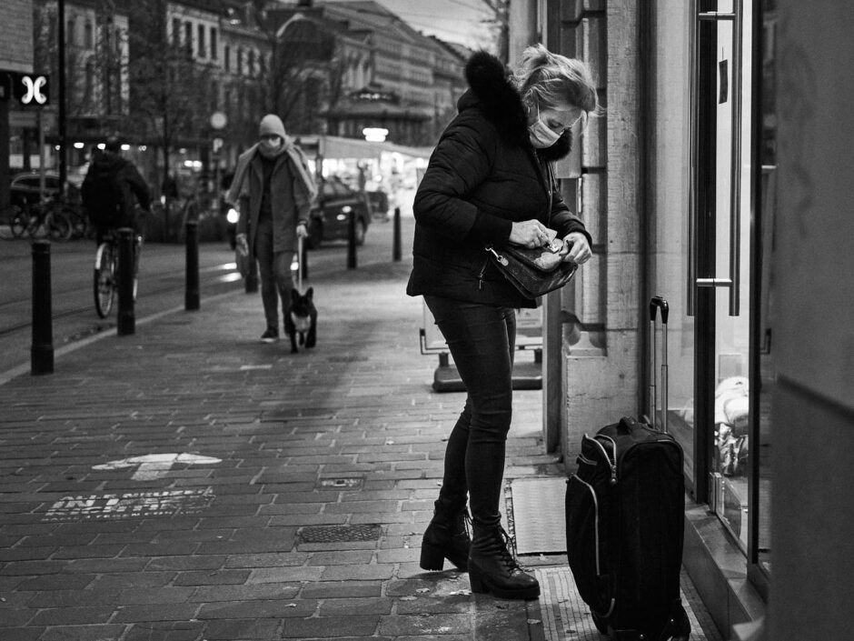 Black & white street photography of homo urbanus, more precisely of a young woman with a suitcase at the front door of a house at dusk