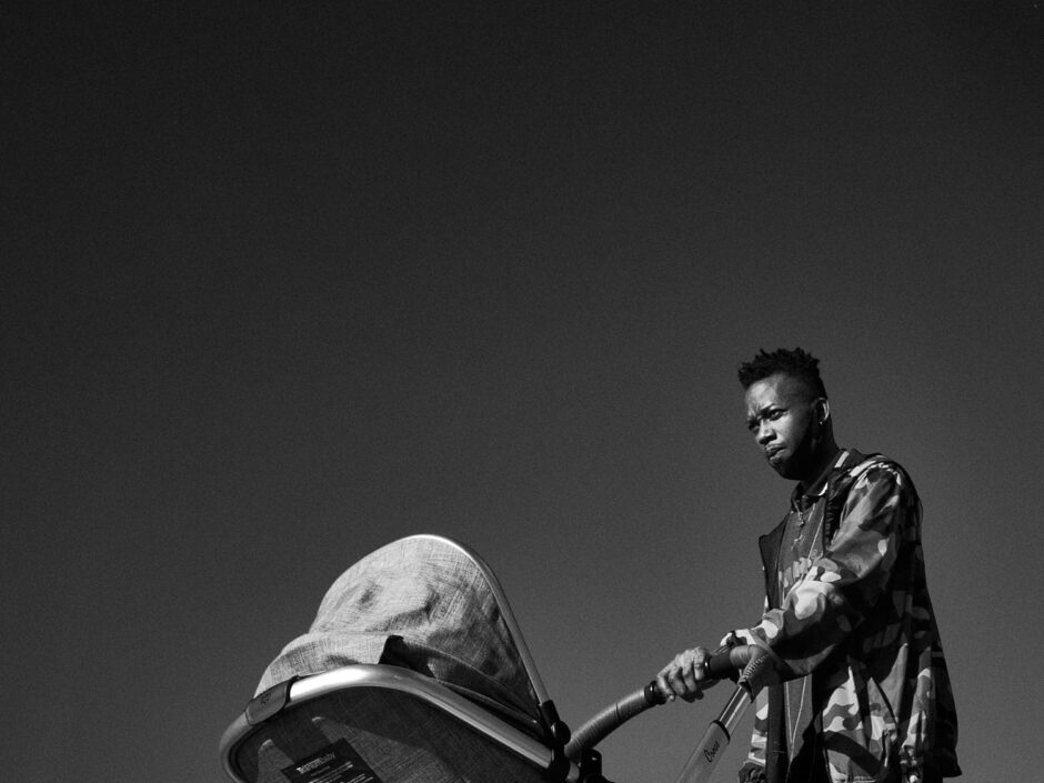 Black & white street photography of homo urbanus, more precisely of a young father pushing his pram in front of a blue sky backdrop