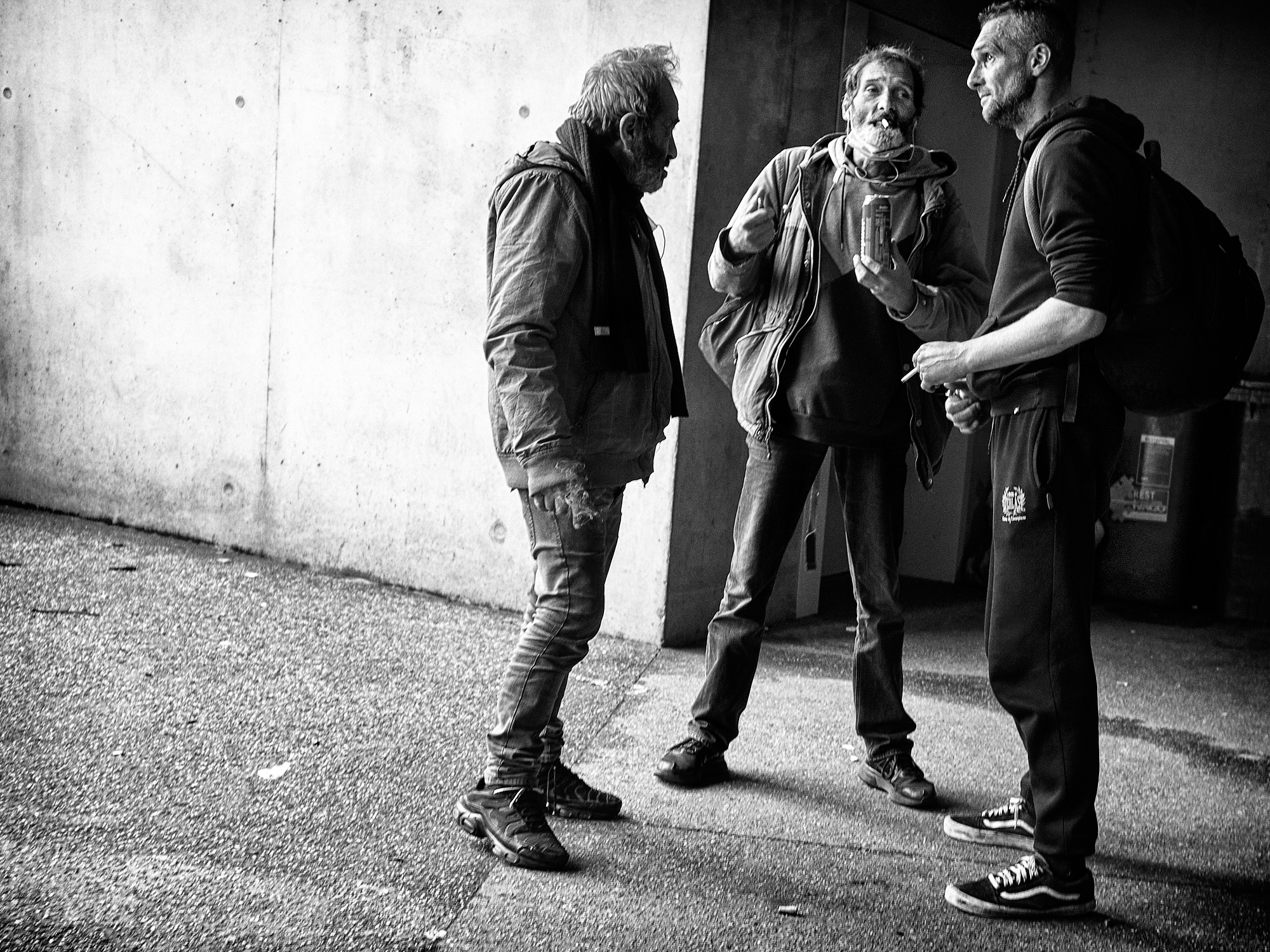 Black & white photograph of a three young man gathering for a smoke and a drink