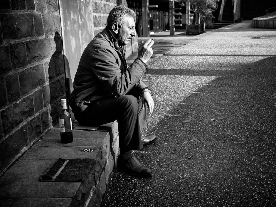 Black & white photograph of middle-aged man with a cigaret and a bottle of wine, waiting for a friend