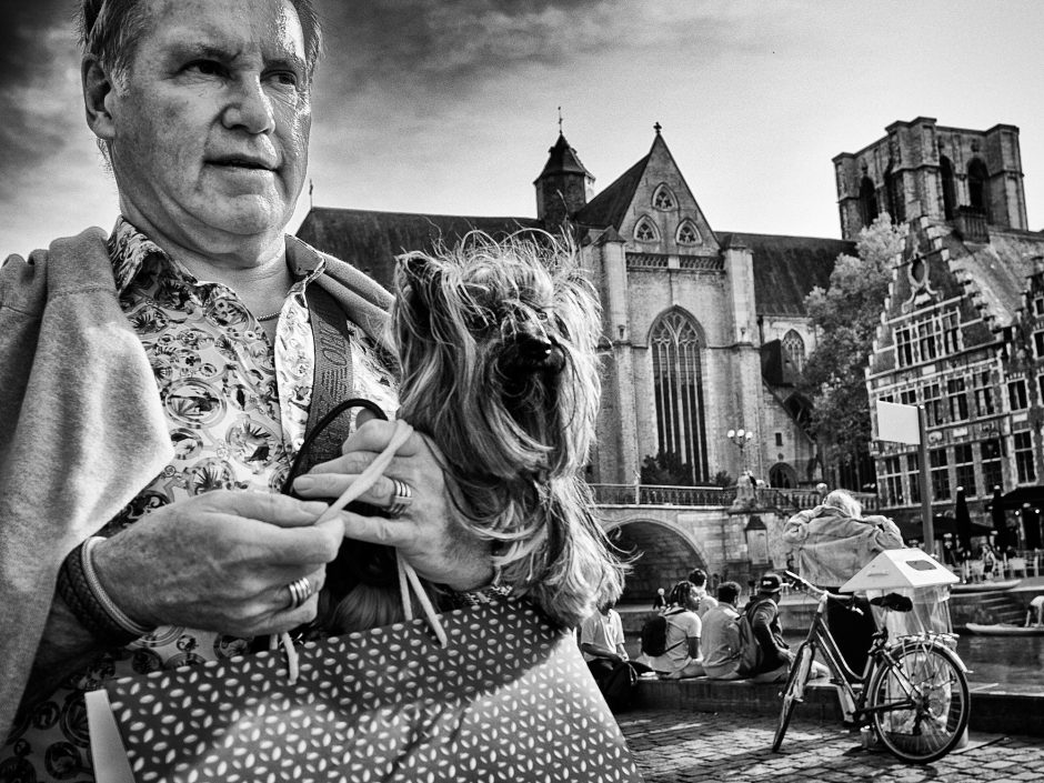 Black & white photograph of a man with a shoulder bag and a yorkshire terrier in his arms