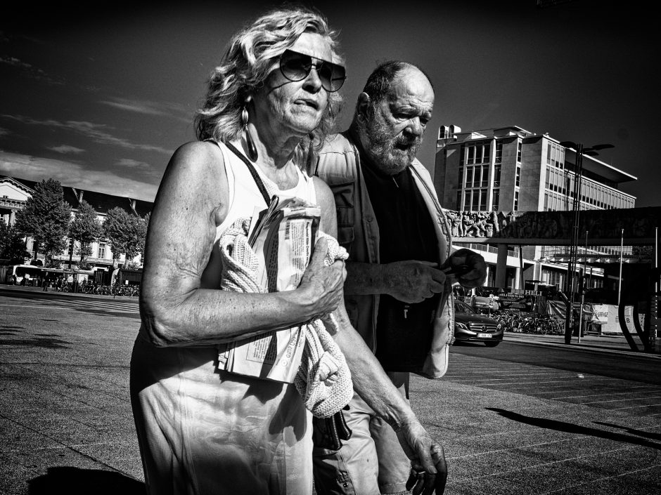 Black & white photograph of a middle aged couple on a hot day. The lady is licking her lips in concentration or thirst.