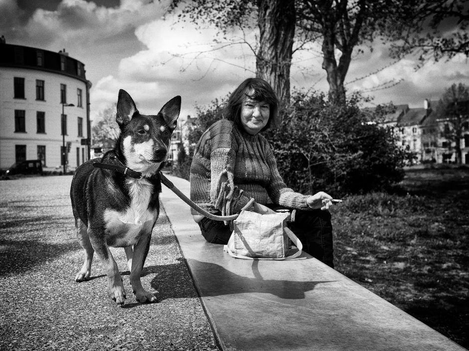 Black & white photograph of a lady taking a break and enjoying a cigaret while her dog is standing guard