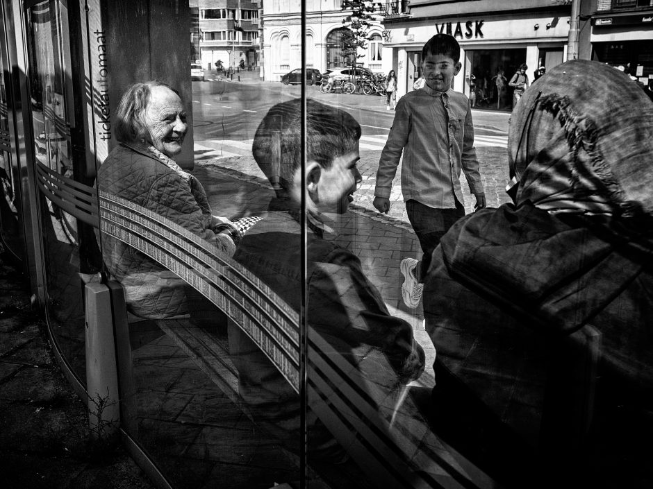 Black & white photograph of a elderly lady socializing with a young mother and her son in a bus stop