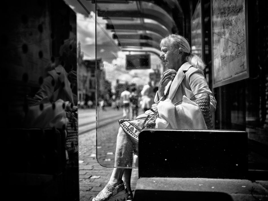 Black & white photograph of a middle aged woman with a melancholic look in a bus stop,